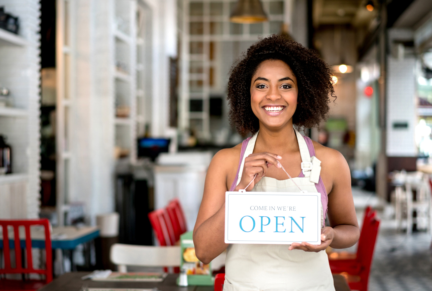 Sonriente mujer propietaria de negocio sosteniendo un cartel de abierto en un restaurante
